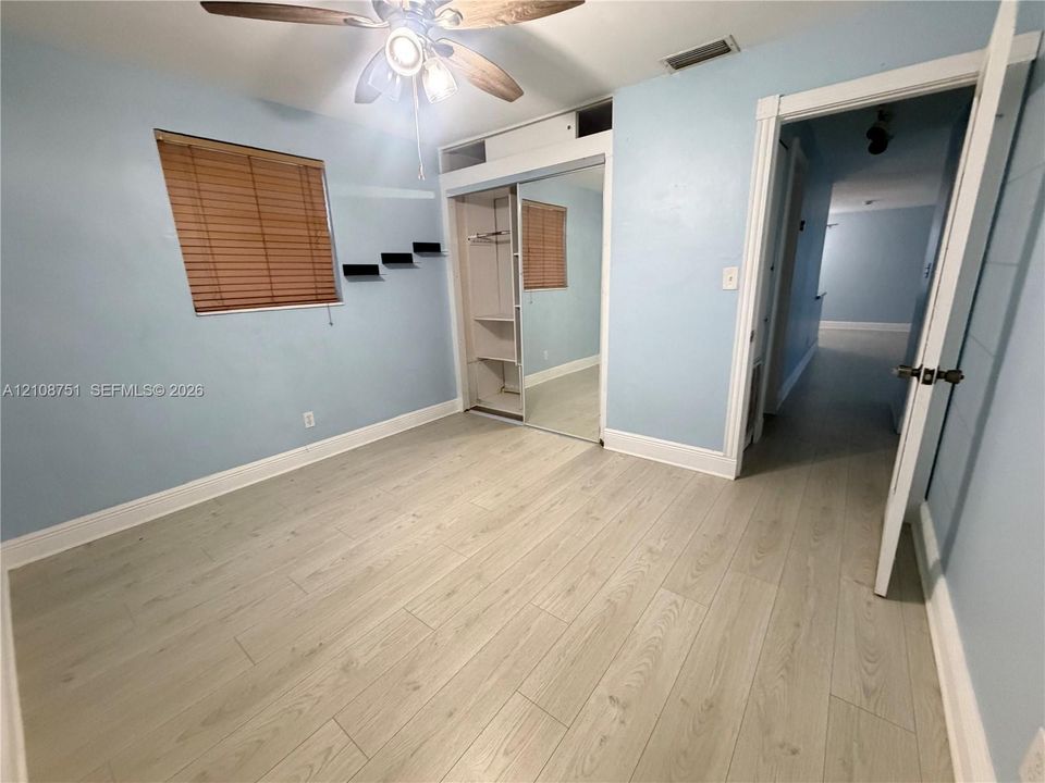 Wood-finish flooring, ceiling fan with integrated lighting, and closet featuring mirrored sliding doors with built-in shelving