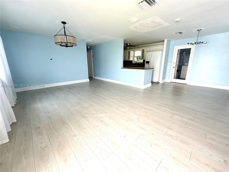 Open-concept living space featuring wood-finish flooring, a tiered kitchen peninsula with a stone-top surface, two drum-style pendant light fixtures, and a glass-panel entry door