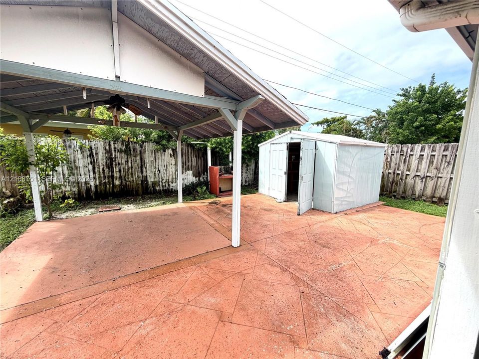 Stamped concrete patio featuring a covered pavilion, ceiling fan, and detached storage structure, enclosed by perimeter wood fencing