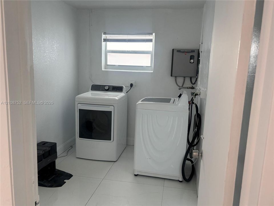 Laundry area featuring neutral-toned tile flooring, white walls, and a window with blinds