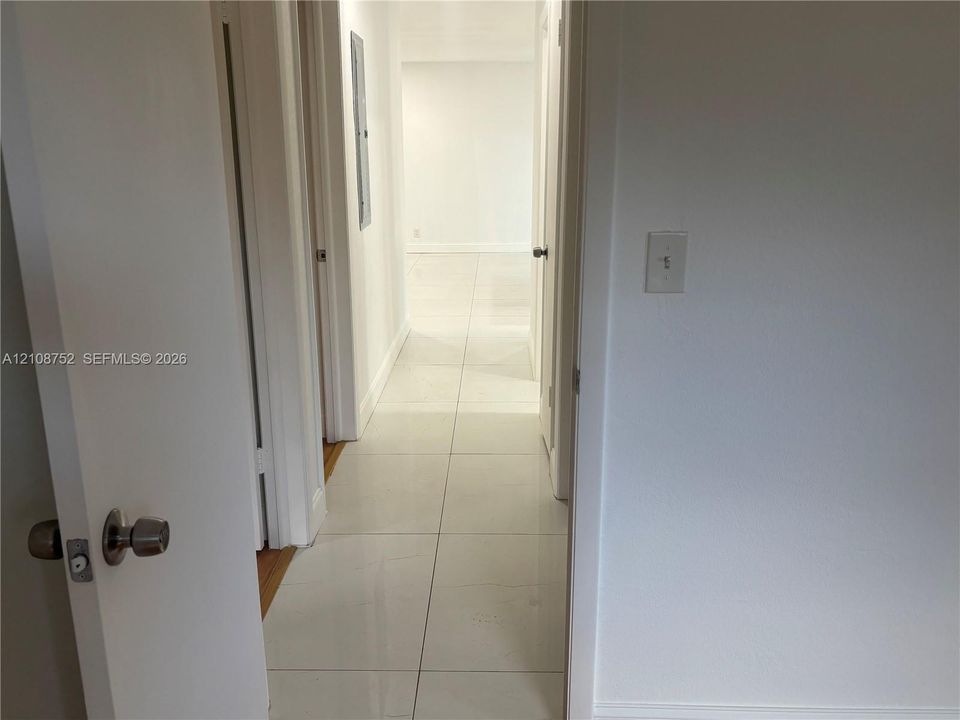 Interior hallway featuring large-format ceramic tile flooring, neutral wall finishes, and solid-core interior doors with satin nickel hardware