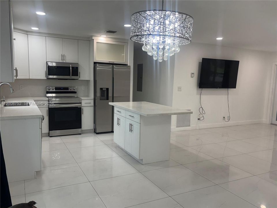 Kitchen featuring white shaker-style cabinetry, quartz countertops, stainless steel appliances, a central island, and large-format tile flooring