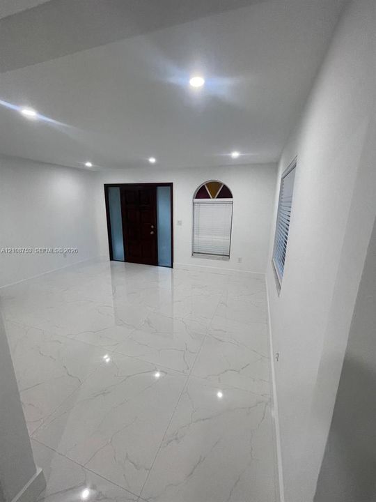 Large-format, high-gloss polished tile flooring featuring natural veining, recessed ceiling lighting, arched window with decorative accent, and dark-finish front entry door with frosted glass side panels