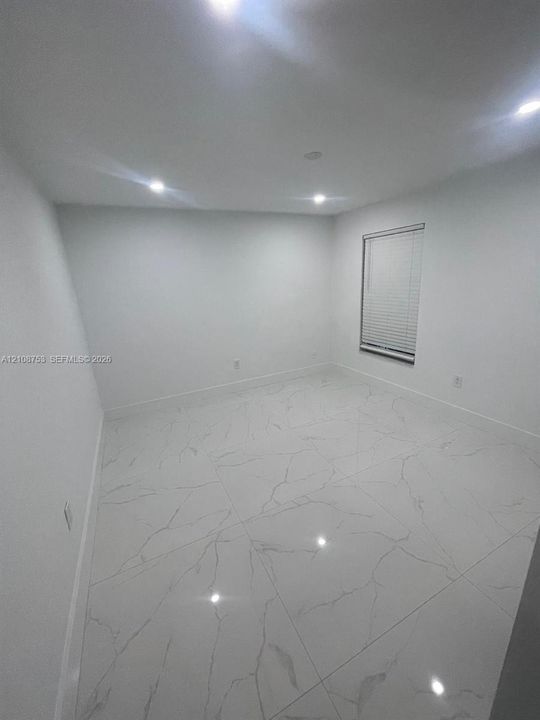 Large-format stone-style tile flooring with veining detail, recessed ceiling lighting, and a single window with horizontal blinds