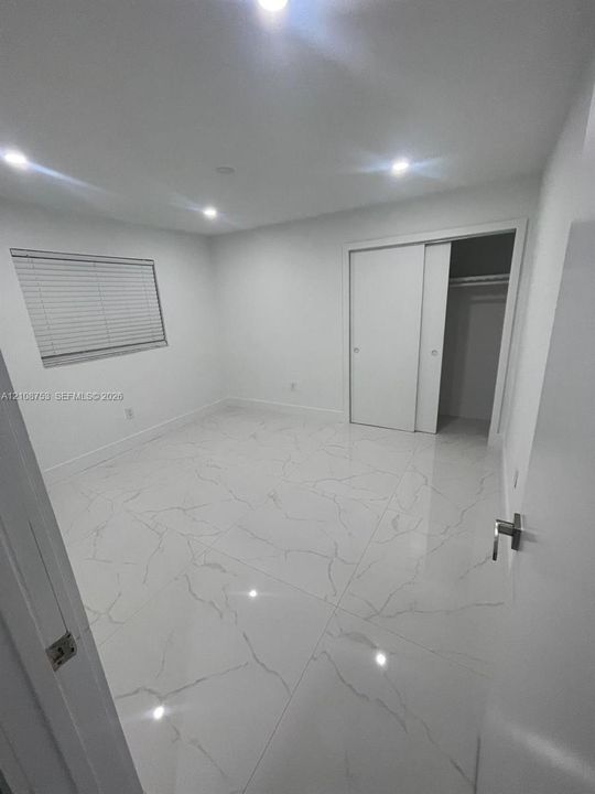 Large-format polished porcelain tile flooring, recessed LED lighting, sliding-door closet, and window with horizontal blinds