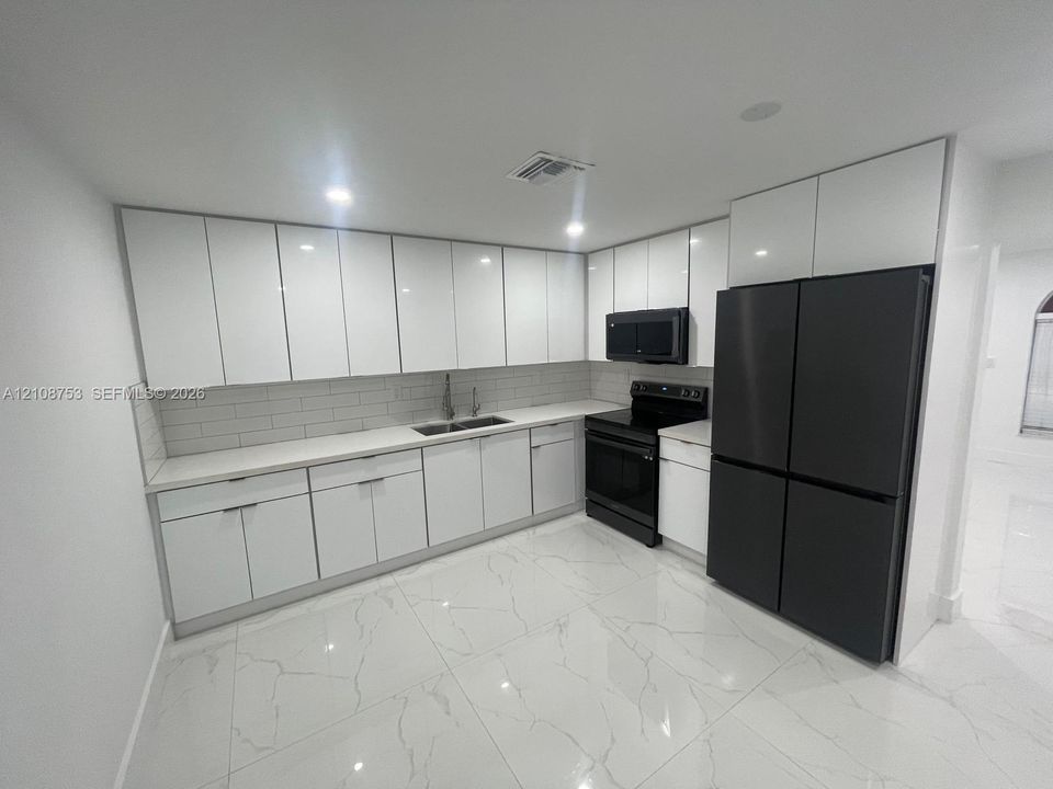 Kitchen featuring gloss-finish white cabinetry, stone-surface countertops, subway tile backsplash, oversized light-colored floor tiles with vein detailing, and integrated black appliances
