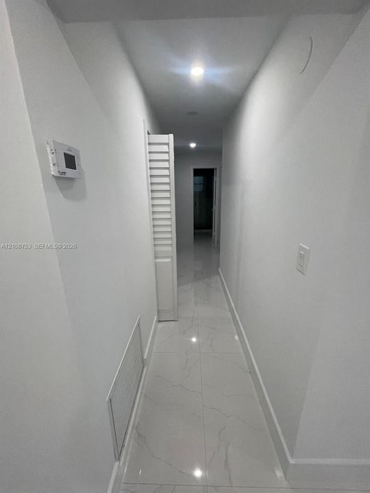Hallway featuring large-format porcelain tile flooring, recessed ceiling lighting, and a white louvered bifold door