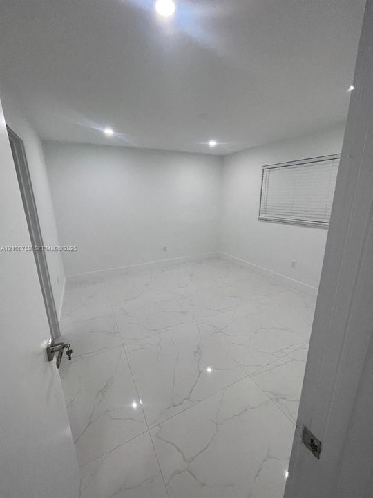 Large-format rectified tile flooring with veining detail, recessed ceiling lighting, and horizontal window blinds