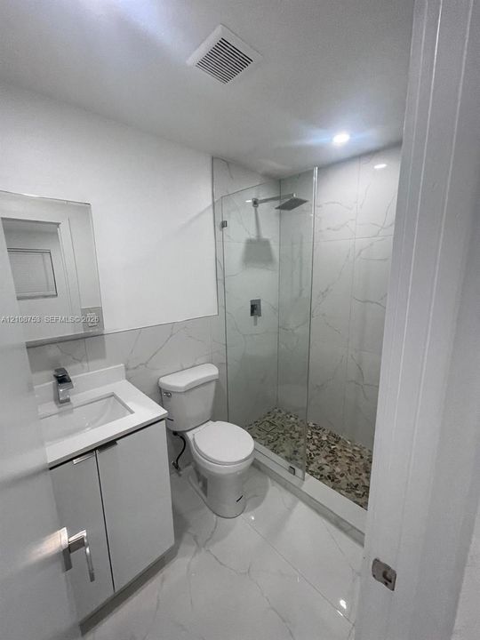 Modern bathroom featuring a glass-enclosed shower with a stone-pebble floor, large-format tile surround, white vanity with a quartz countertop, and rectangular undermount sink