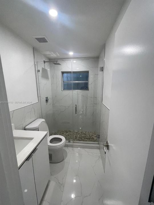 Bathroom featuring floor-to-ceiling large-format veined tile, walk-in shower with a glass enclosure, river stone shower floor, and a white vanity with an integrated basin