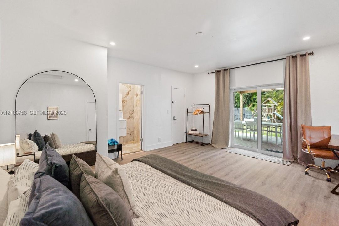 Neutral interior featuring wood-finish flooring, recessed lighting, a large arched mirror, and sliding glass doors with direct exterior access