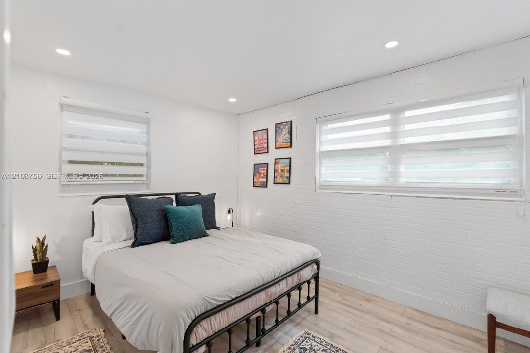 Bright interior featuring white painted brick walls, wood-finish flooring, recessed lighting, and dual windows with fitted shades