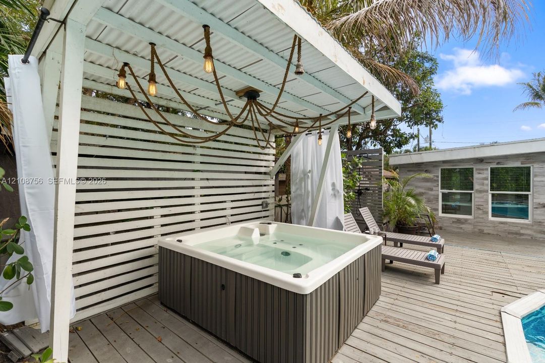 Outdoor space featuring a covered hot tub, horizontal slat privacy screen, suspended pendant lighting, and wood decking