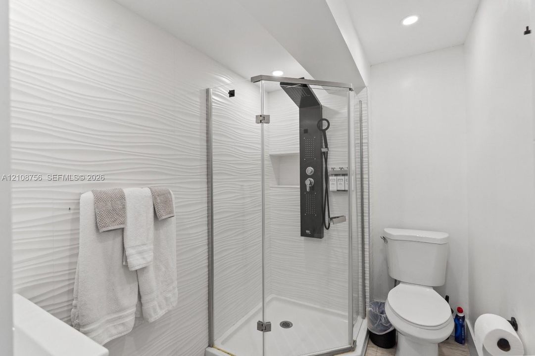Corner glass shower enclosure featuring a multi-jet shower panel, recessed wall niche, and white textured tile surround