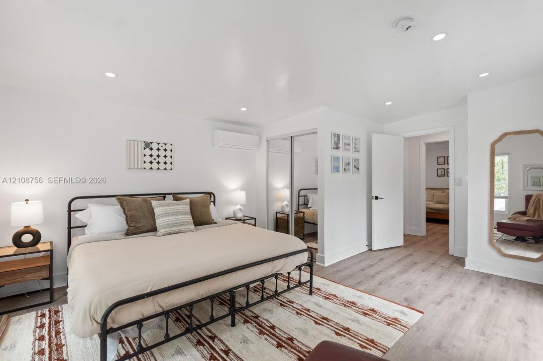 Room featuring wood-finish flooring, recessed lighting, wall-mounted ductless air conditioning unit, and sliding mirror-paneled closet doors
