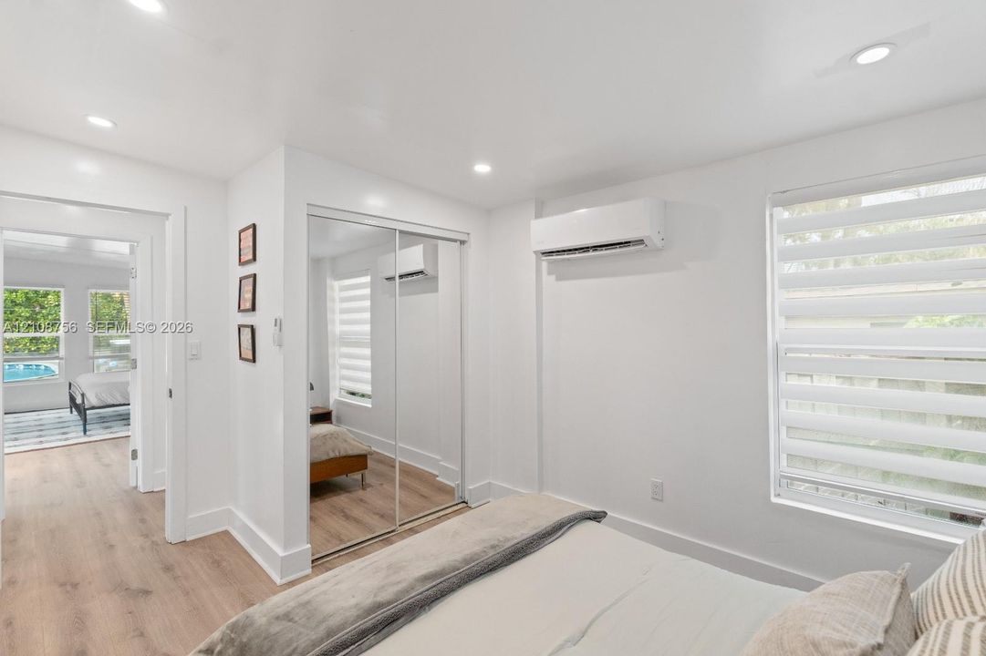 Bedroom featuring wood-finish flooring, recessed lighting, wall-mounted ductless air conditioning unit, and sliding mirrored closet doors