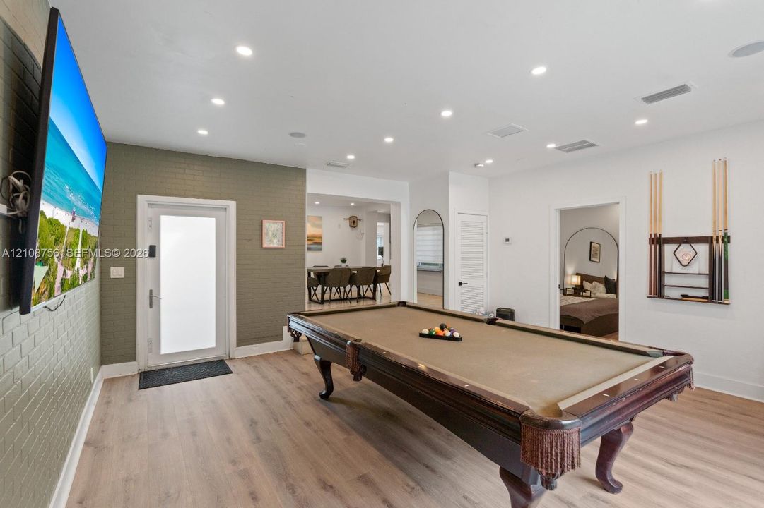 Recessed ceiling lighting, wood-finish flooring, and an olive-toned brick accent wall featuring an exterior door with a frosted glass pane