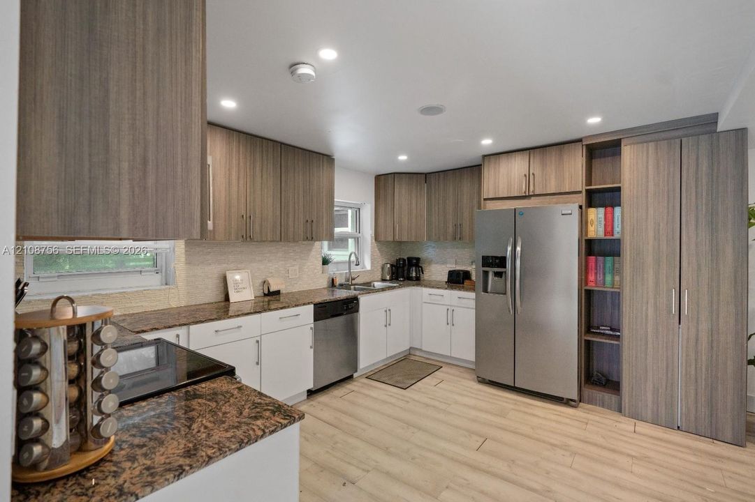 Kitchen featuring two-tone cabinetry with wood-finish uppers and white base units, stone countertops, stainless steel appliances, built-in shelving, and light-toned flooring