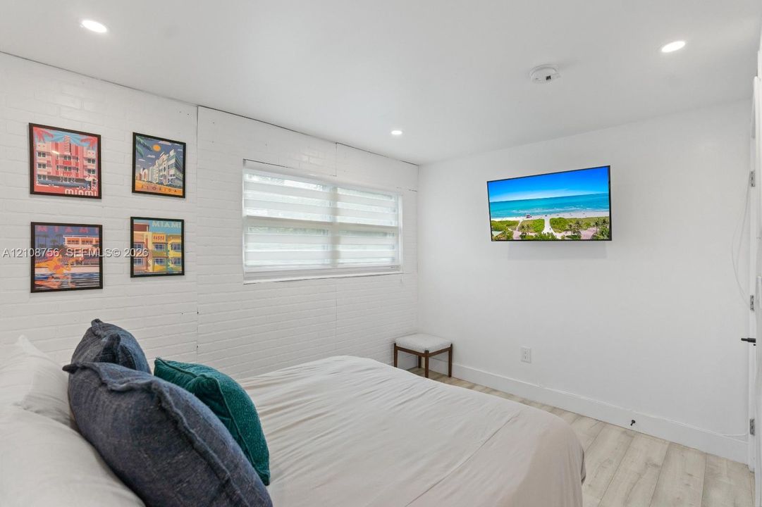 Painted brick wall texture, light-toned wood-finish flooring, recessed lighting, and dual-layered window shades