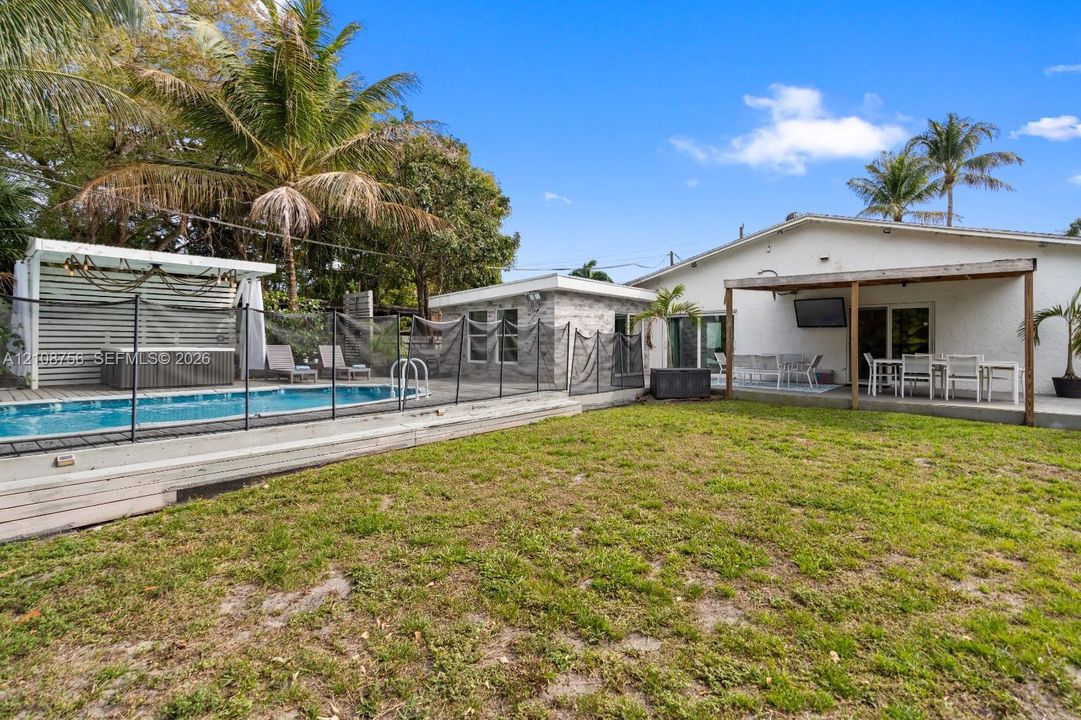 Rear exterior featuring a swimming pool, detached structure with stone-finish exterior, covered patio, wood-finish pergola, and lawn space