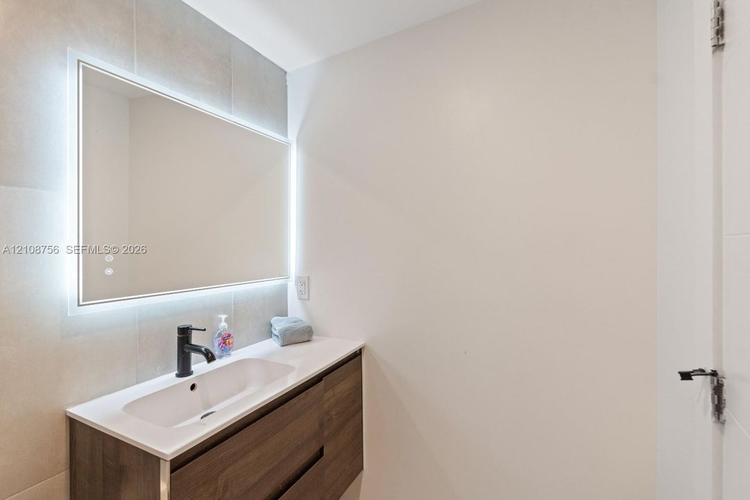 Floating wood-finish vanity with integrated sink, rectangular LED-backlit mirror, and matte black faucet fixture