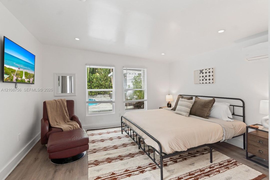 Neutral-toned room featuring wood-finish flooring, recessed lighting, dual windows with blinds, and a wall-mounted climate control unit