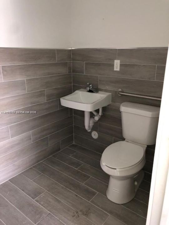 Wall-mounted sink with chrome-finish faucet, wood-finish tile flooring, coordinating horizontal wall tiling, and metal grab bar