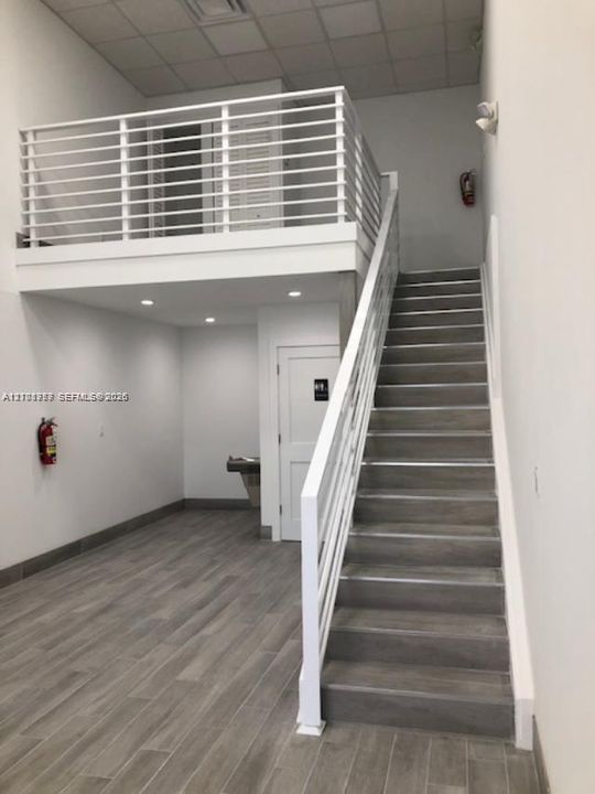 Interior space featuring wood-finish tile flooring, a mezzanine level with white metal railings, recessed lighting, and a staircase with metal railings