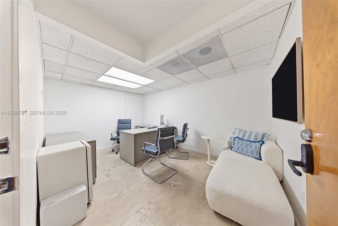 Interior room featuring recessed tray ceiling, drop ceiling panels, large-format tile flooring, and a door with a matte black electronic keypad lock