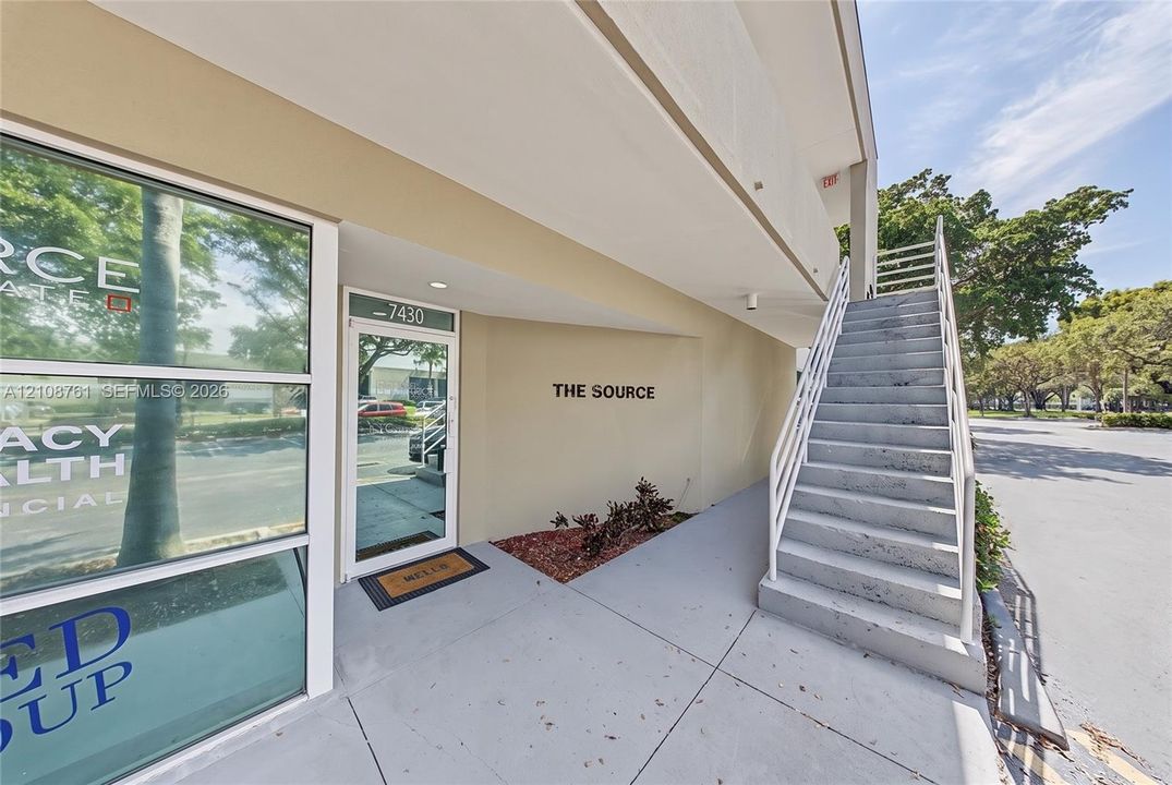 Exterior entrance featuring a glass-paneled storefront door, concrete staircase with metal railings, and recessed ceiling lighting