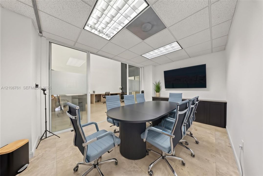 Conference room featuring neutral tile flooring, drop ceiling with recessed lighting panels, dark built-in cabinetry, and a full-height glass wall partition