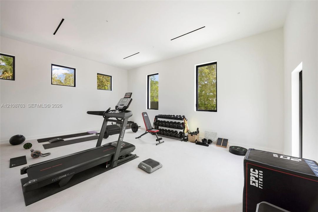 Spacious interior room with high ceilings, neutral wall finishes, recessed linear lighting, and multiple window installations with black frames