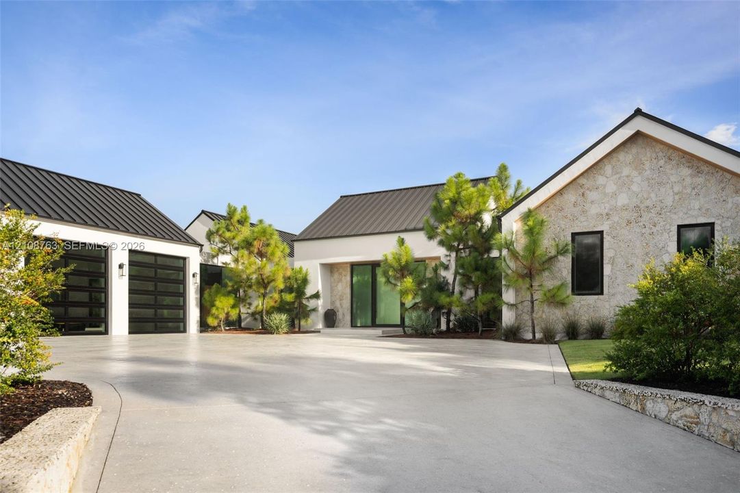 Modern exterior featuring stone facade, standing-seam metal roofing, concrete driveway, and multi-panel glass garage doors