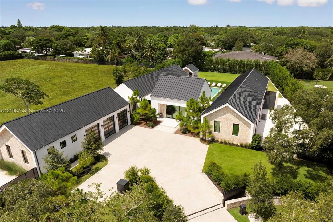 Modern estate featuring a metal roof, stone exterior, three-car garage with glass panel doors, private swimming pool, and extensive grounds