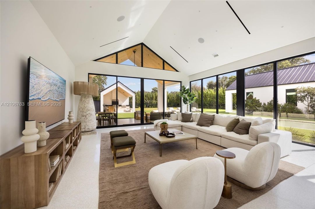 Great room featuring a vaulted ceiling with exposed wood accents, expansive floor-to-ceiling black-framed windows, and light-toned flooring