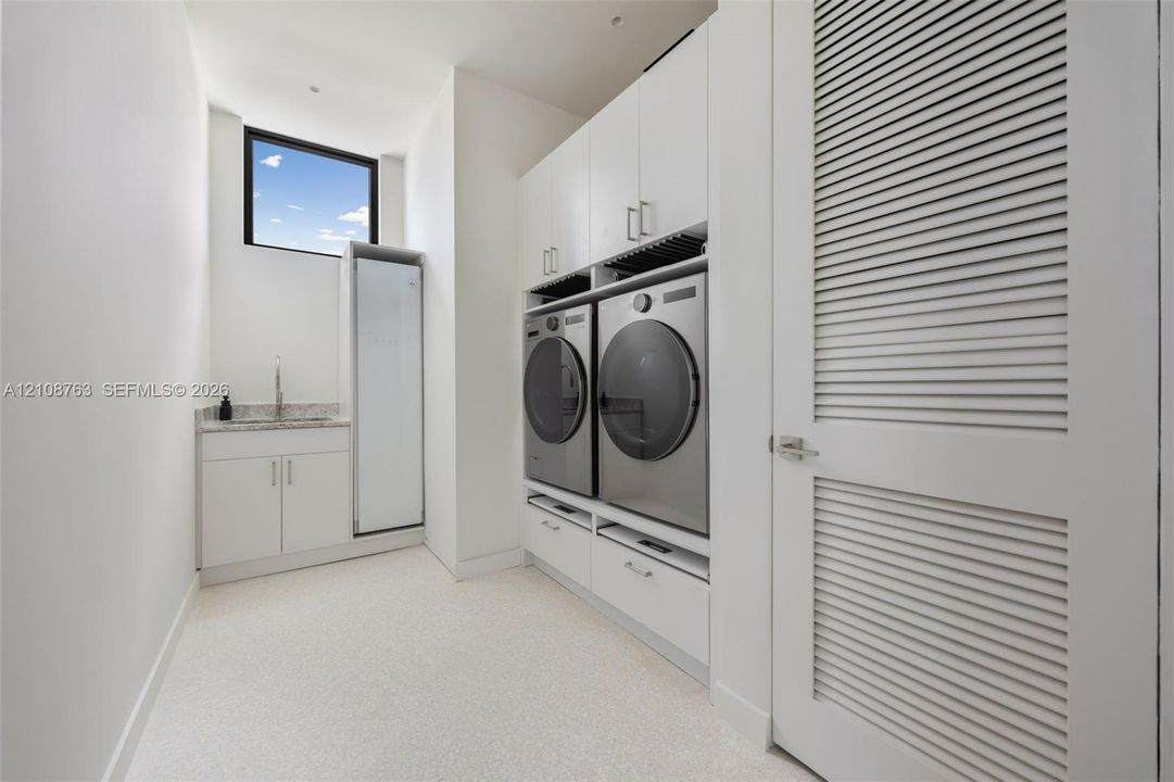 Utility room featuring white shaker-style cabinetry, stone-finish countertops, an integrated basin, high-reach cabinetry, and a louvered door
