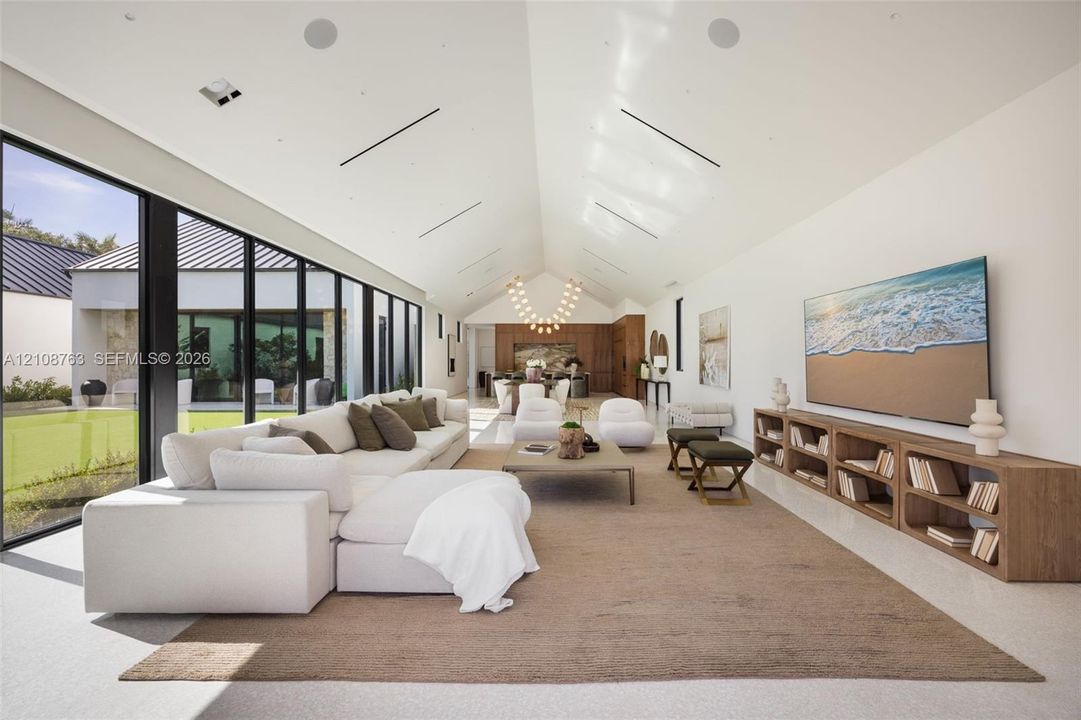 Vaulted ceilings featuring recessed linear lighting, floor-to-ceiling glass wall, built-in wooden media console, and integrated ceiling speakers