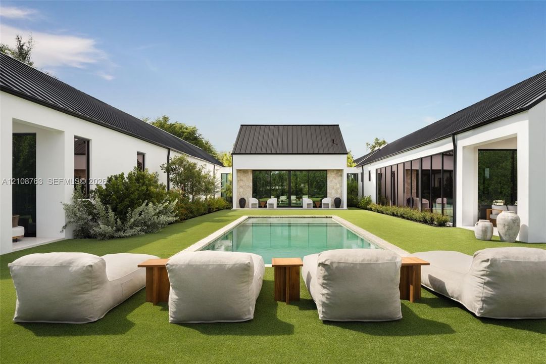 Courtyard layout featuring a rectangular swimming pool, metal roofing, crisp white stucco exterior, expansive glass wall panels, and textured stone masonry accents