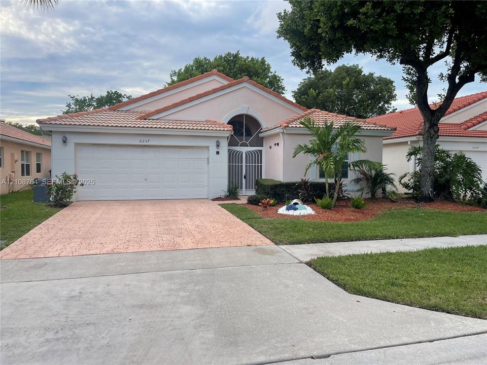 Single-story residence featuring a terracotta-tiled roof, decorative arched entryway with a security gate, two-car garage, and textured paver driveway