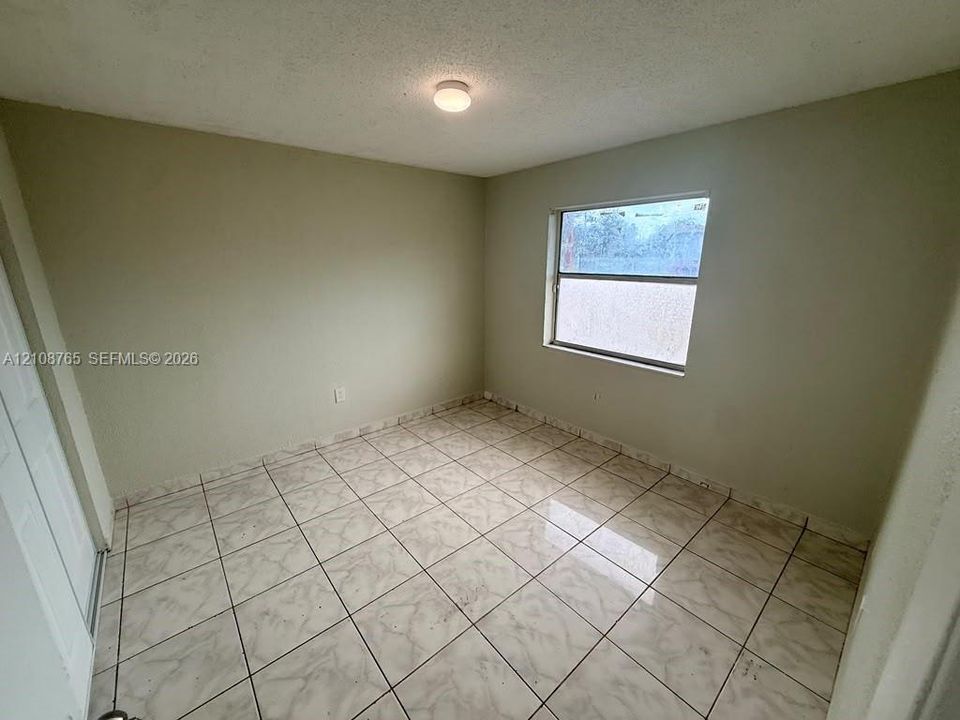 Room featuring neutral-toned walls, tiled flooring, a single-pane window, and a central ceiling-mounted light fixture