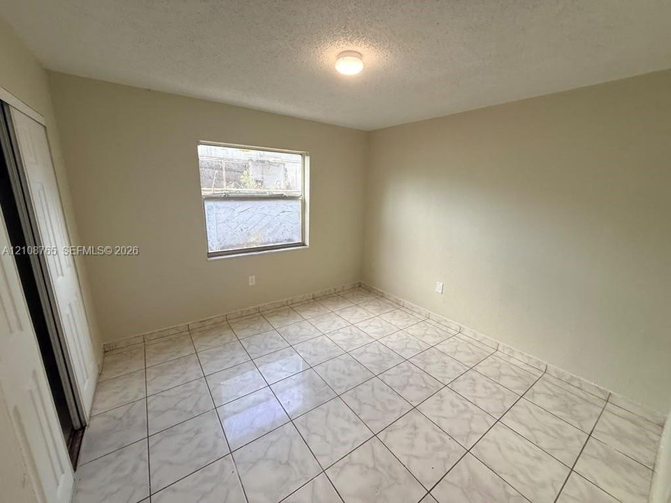 Neutral interior featuring large-format tile flooring, a window with natural light, and a built-in closet with paneled sliding doors