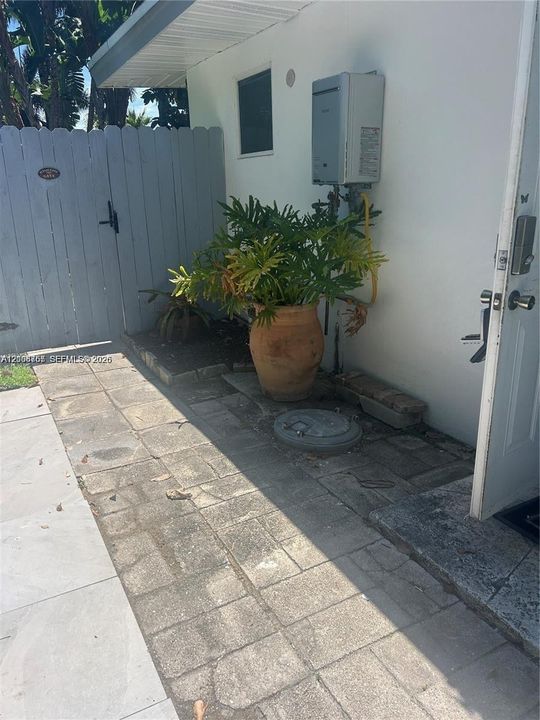 Exterior area featuring paver-stone hardscaping, wall-mounted tankless water heater, and a white privacy fence