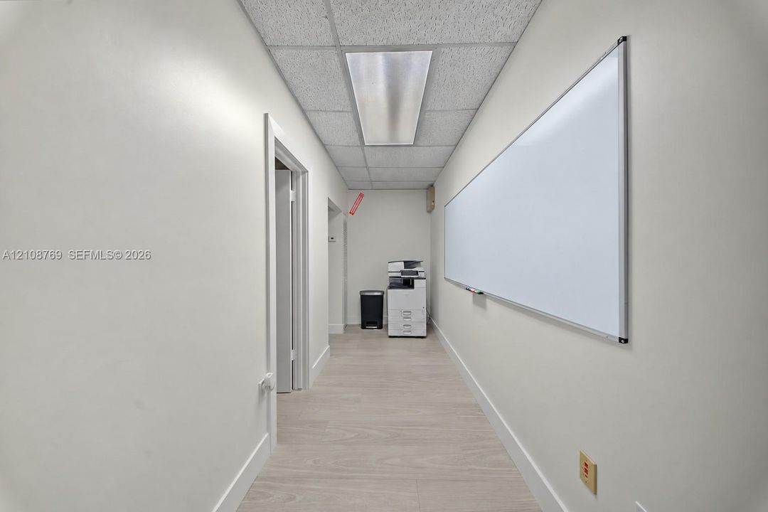 Hallway featuring wood-finish flooring, suspended grid ceiling, recessed linear lighting, and a wall-mounted dry-erase board