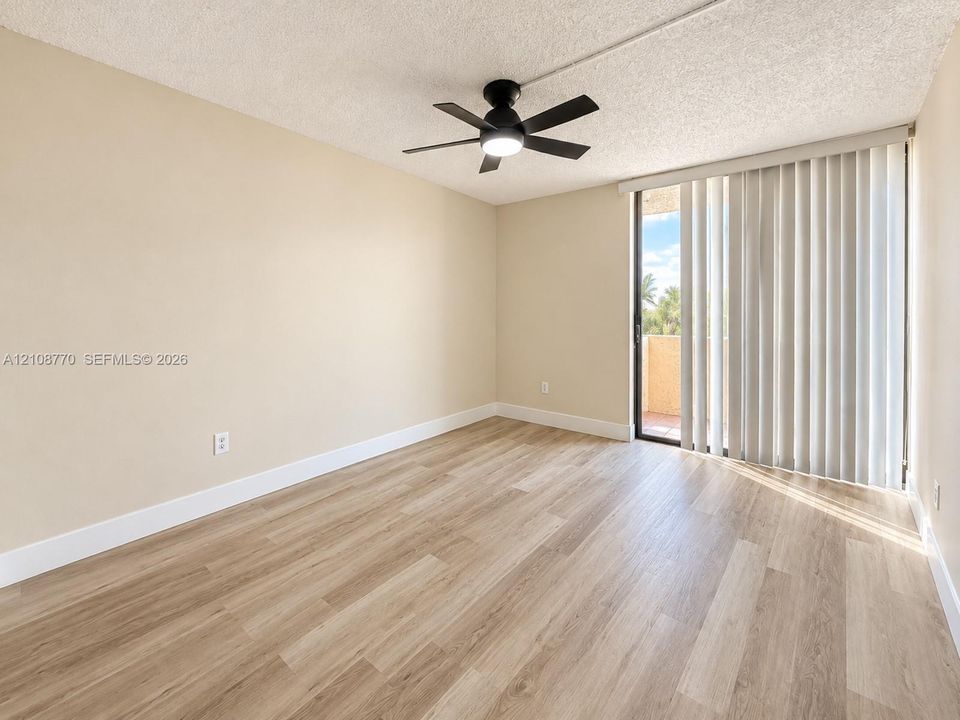Room featuring wood-finish flooring, a matte black ceiling fan with an integrated light fixture, and a sliding glass door with vertical blinds