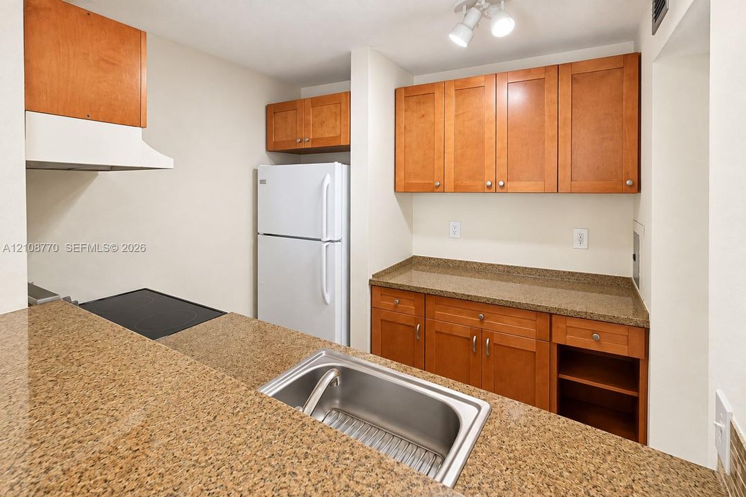 Kitchen featuring wood-finish cabinetry, solid surface countertops, stainless steel sink, and integrated overhead lighting