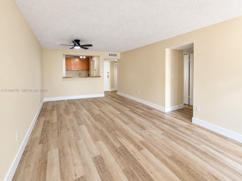 Wood-finish flooring throughout, matte black ceiling fan, pass-through opening to kitchen with wood cabinetry, and neutral wall tones