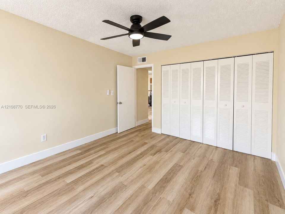 Room featuring wood-finish flooring, a matte black ceiling fan with an integrated light fixture, and floor-to-ceiling louvered closet doors