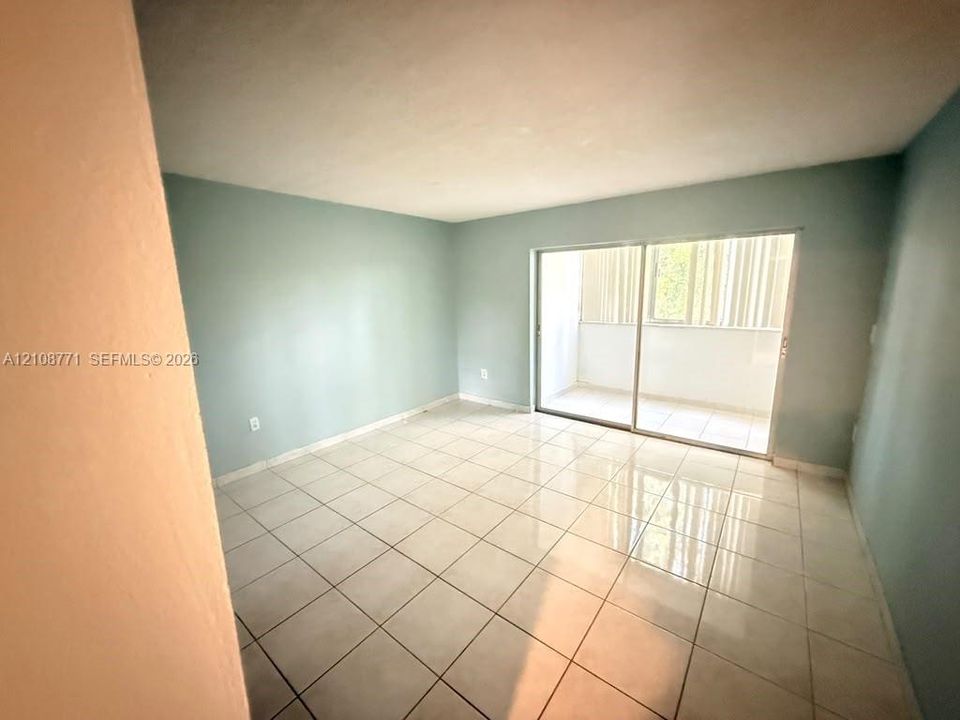 Interior space featuring light-colored tile flooring, neutral wall paint, and floor-to-ceiling sliding glass doors opening to an exterior balcony
