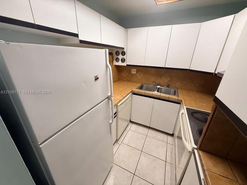 Kitchen featuring flat-panel white cabinetry, tile countertops, square-tile backsplash, double-basin stainless steel sink, and ceramic tile flooring