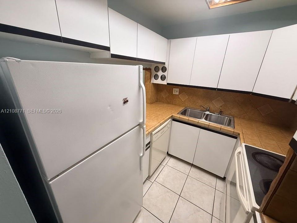 Kitchen featuring white cabinetry, tile countertops, tile backsplash, tile flooring, and a stainless steel double-basin sink
